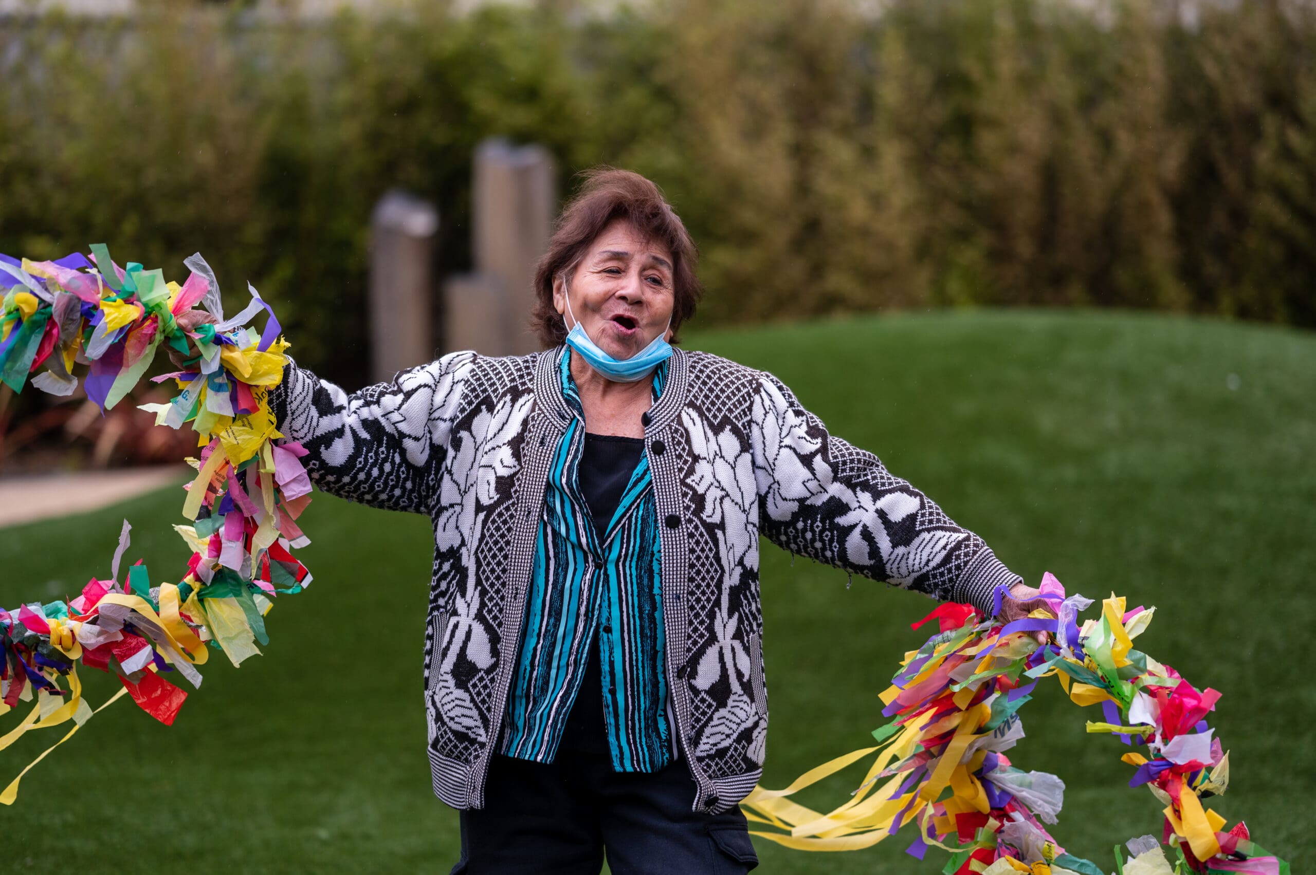 Woman stands outside in front of green hill holding colorful wreaths