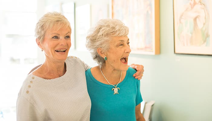 Portrait of two women smiling in front of a wall of artwork at Carlsbad by the Sea