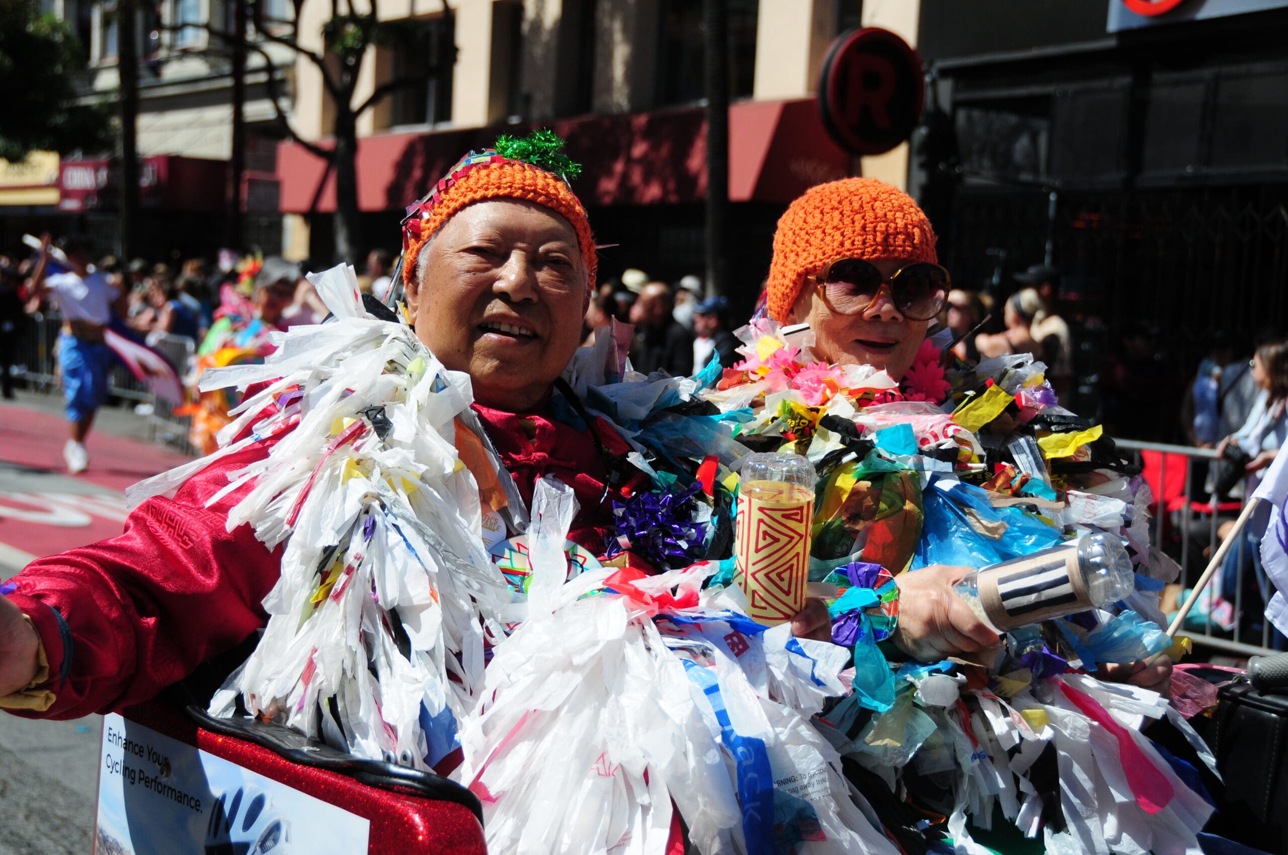 Two older adults in festive attire ride in open car