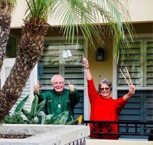 Two residents stand on a balcony holding up drum sticks