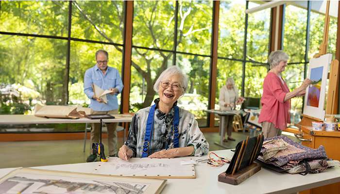 A group of people working on art projects in an art studio with big windows that showcase green trees and natural light.A group of people working on art projects in an art studio with big windows that showcase green trees and natural light.